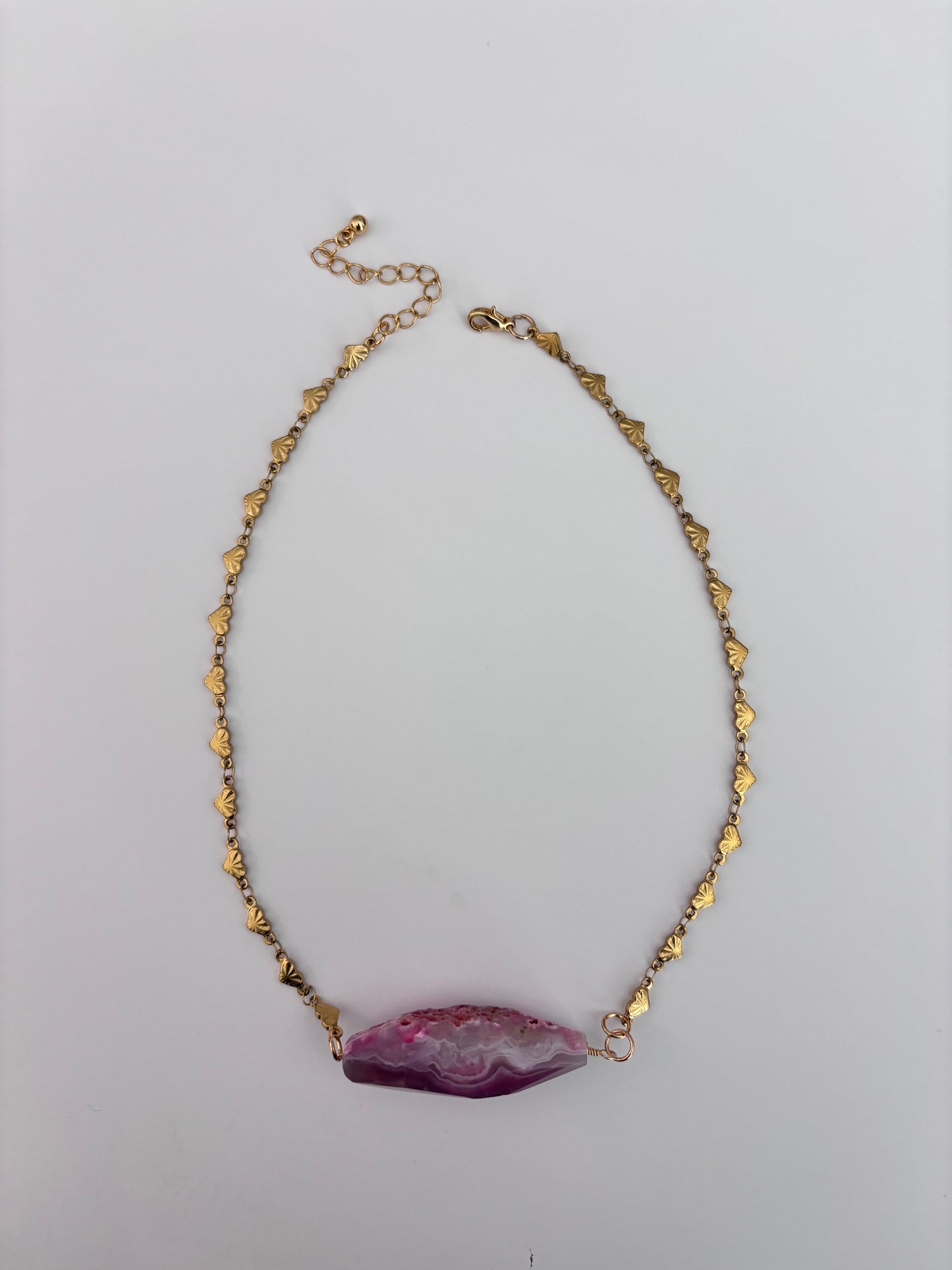 A gold chain necklace with small metallic leaf-shaped charms and a large, polished purple agate geode pendant, displayed on a light gray background.